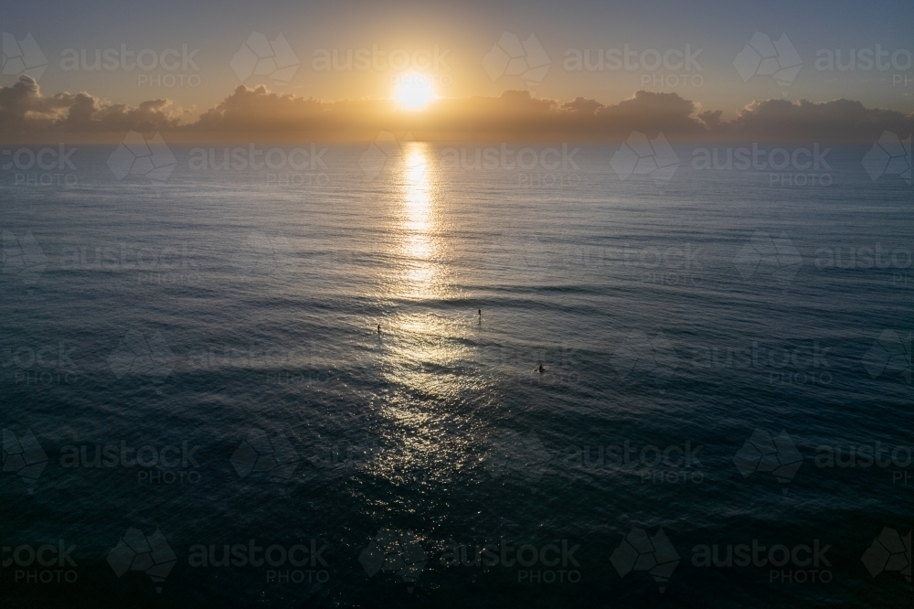 The sunrise over the ocean with paddle boarders waiting for waves - Australian Stock Image