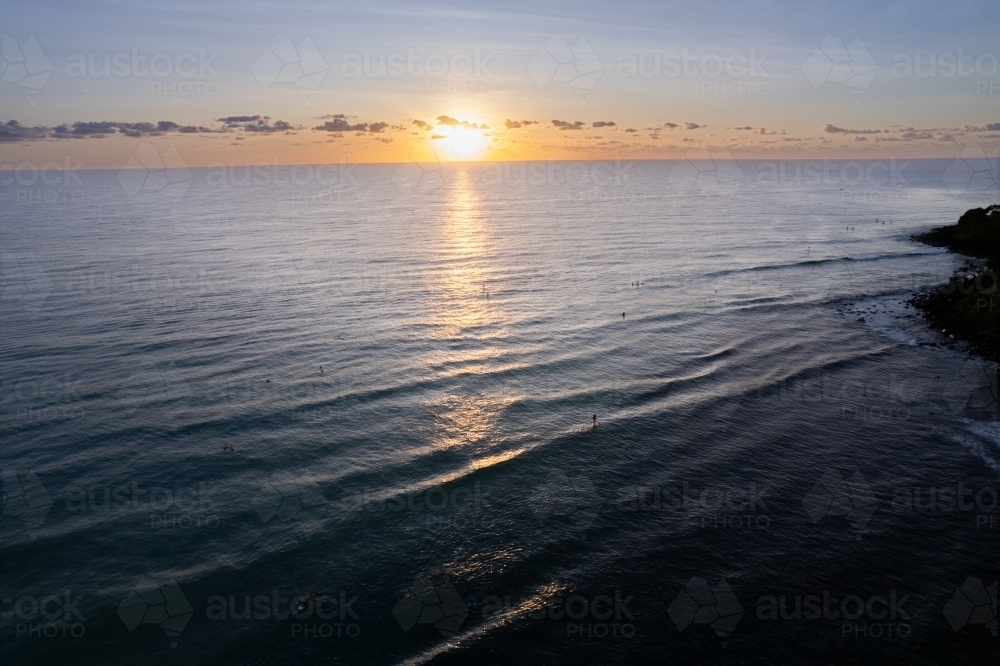The sunrise over the ocean with surfers and paddle boarders waiting for the waves off the coast. - Australian Stock Image