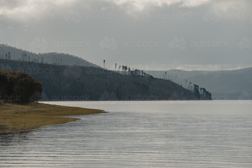 The water's edge with mountains in the background at Blowering Reservoir - Australian Stock Image