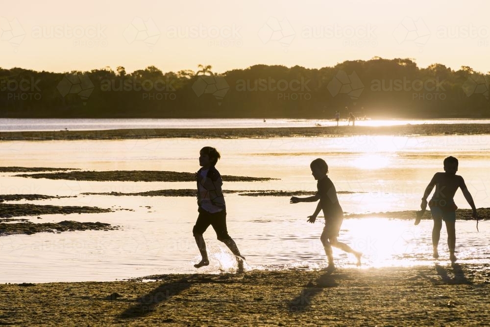 Three boys playing on a beach at sunset. - Australian Stock Image