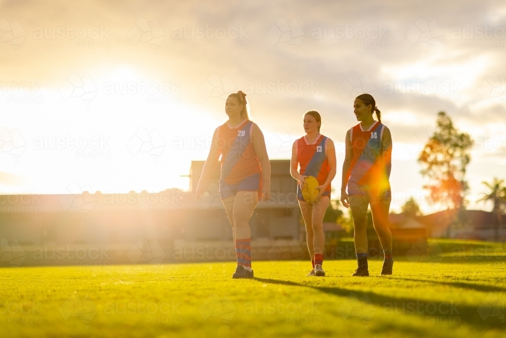 three female football players walking off oval with golden backlight - Australian Stock Image