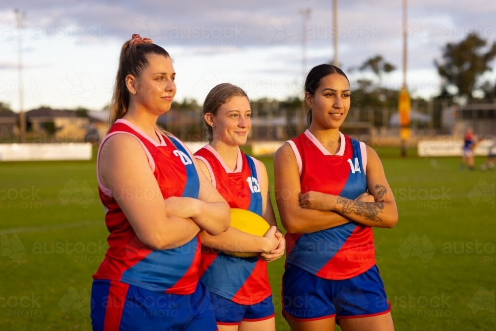 three female footballers standing on oval with arms crossed - Australian Stock Image