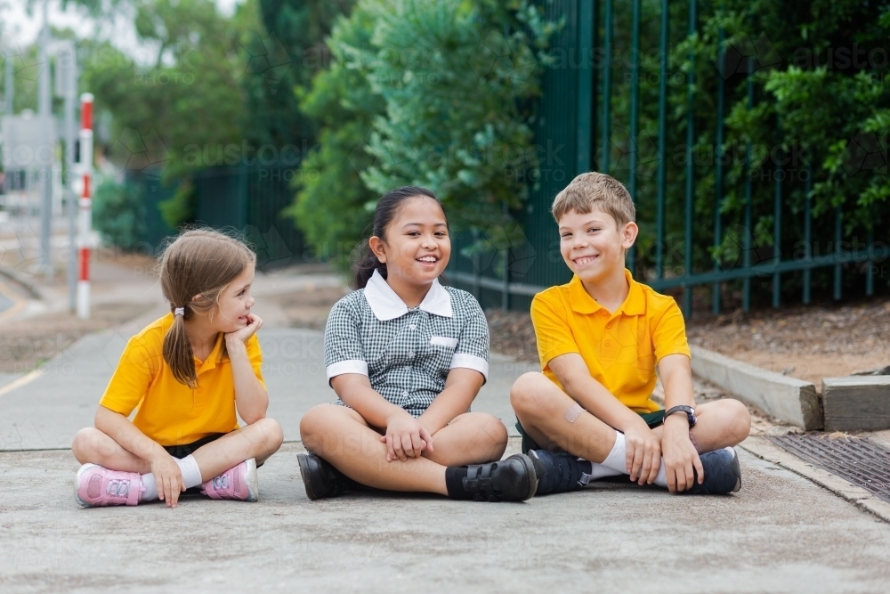 Three happy public school friends in uniform sitting outside - Australian Stock Image