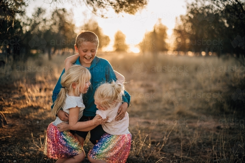 Three kids playing and hugging outside - Australian Stock Image