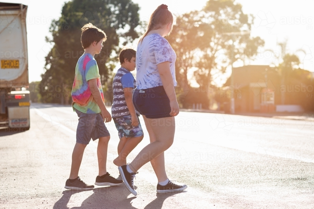 Three kids walking across a road with a truck in the background - Australian Stock Image