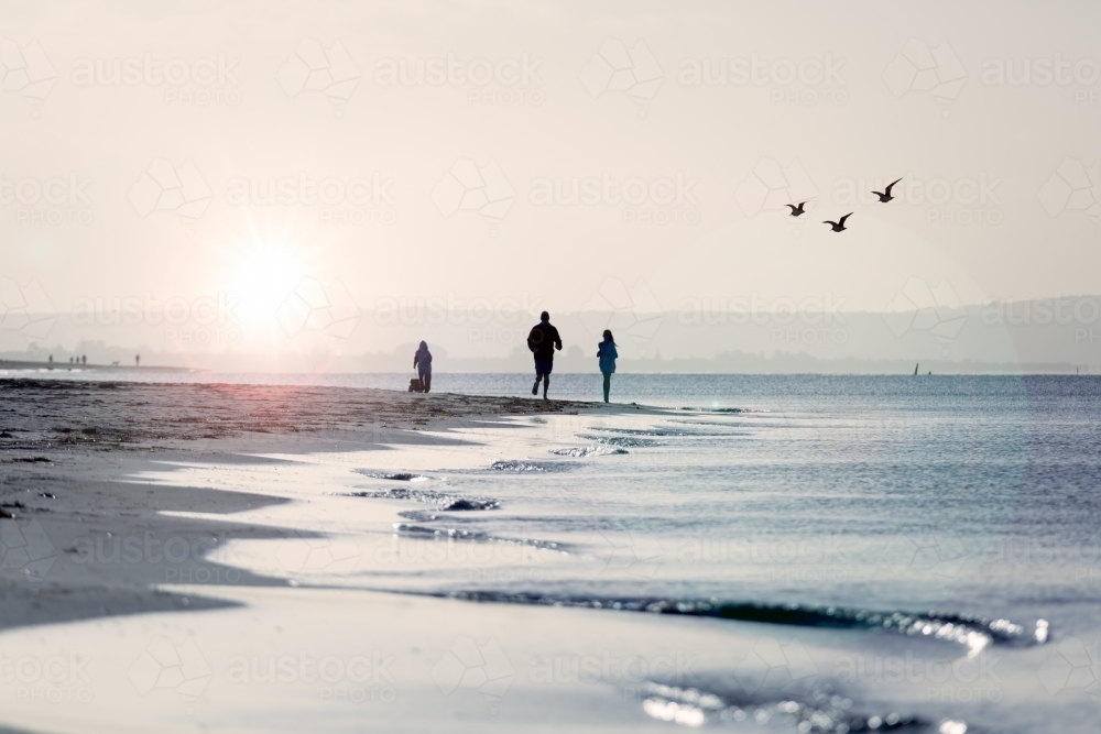 Three people silhouetted on the shoreline of a beach - Australian Stock Image