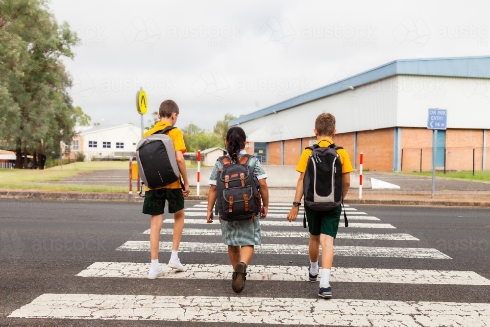 Three public school kids walking to school - crossing the road at a pedestrian crossing - Australian Stock Image