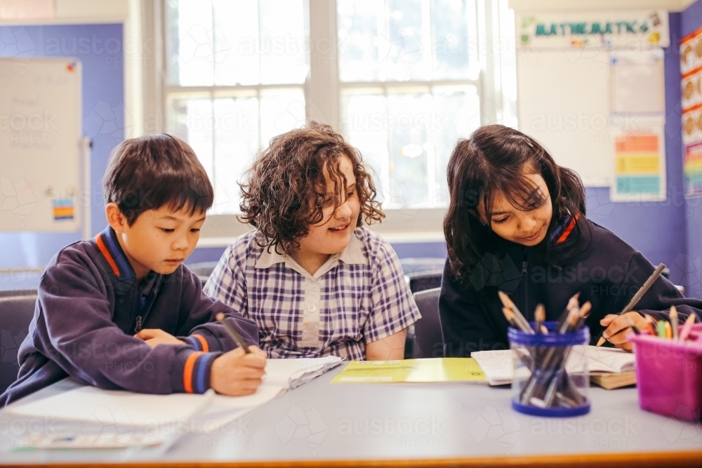 Three school students sitting at their desk in the classroom working - Australian Stock Image