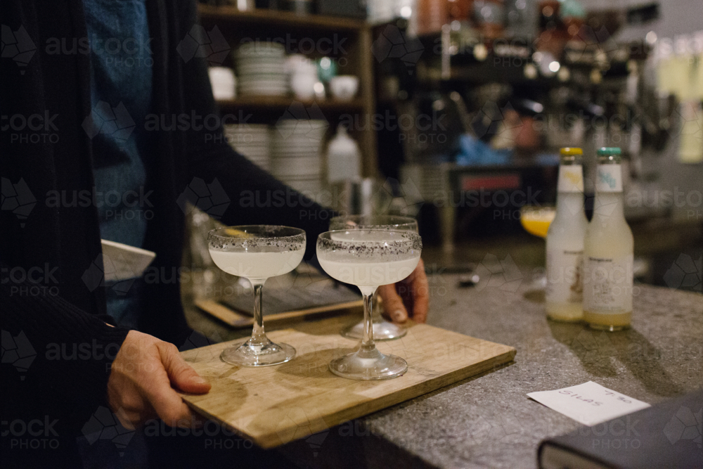 Three stemmed glasses of cocktail served on a wooden board - Australian Stock Image