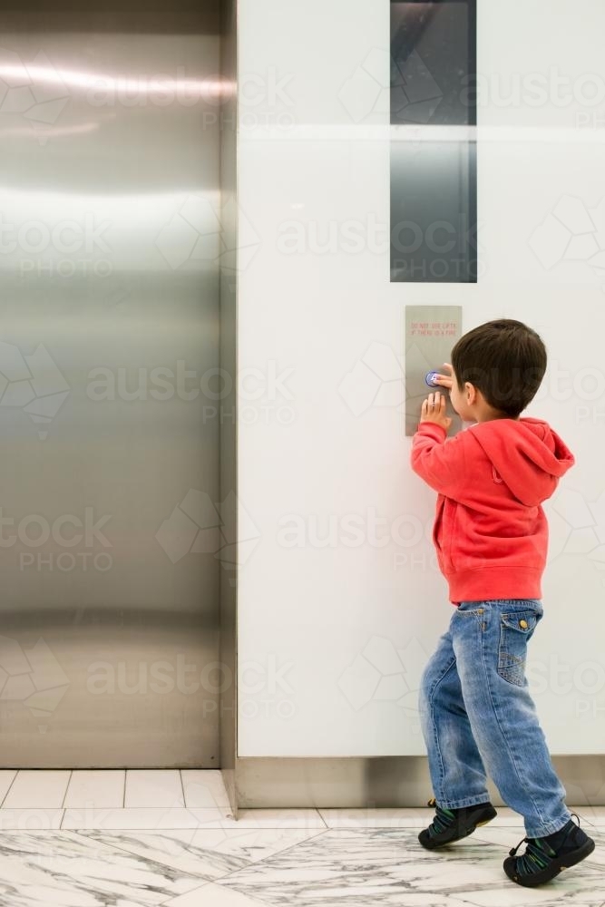 Three year old mixed race boy runs to press a lift button - Australian Stock Image