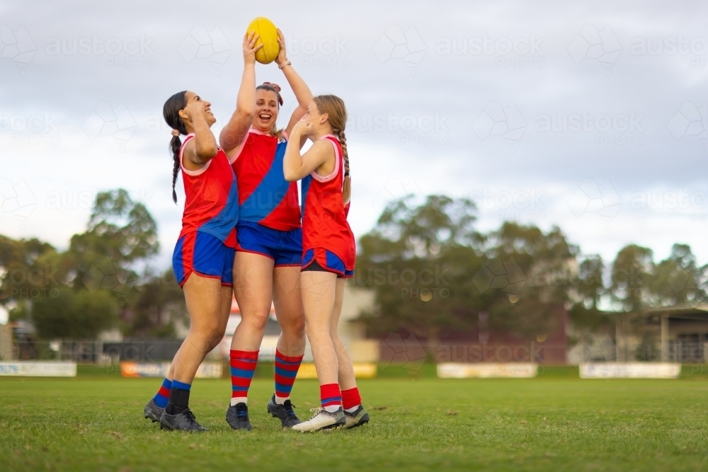 three young women football players in red and blue uniforms with a football - Australian Stock Image
