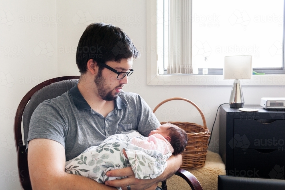 Tired father holding newborn baby daughter in nursery - Australian Stock Image