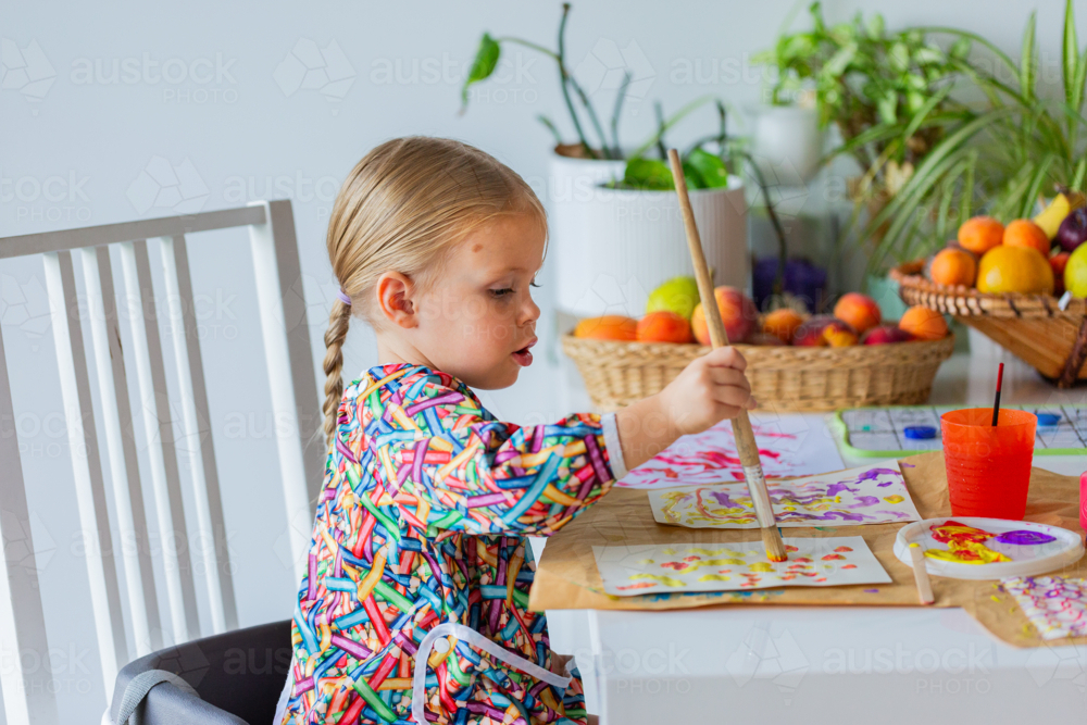 Toddler child at home painting with coloured paint on paper - Australian Stock Image