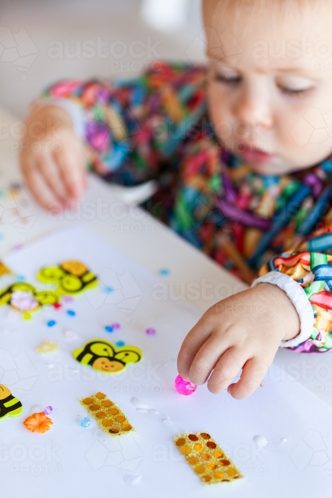 Toddler child in art smock gluing and sticking craft together - Australian Stock Image