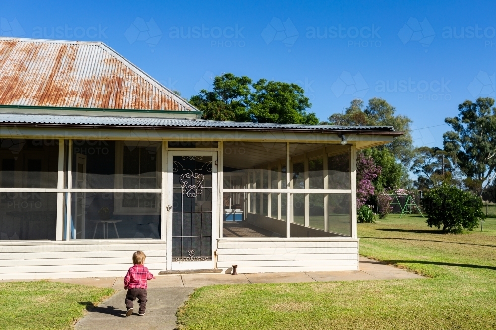 Toddler child walking down path towards farm house homestead - Australian Stock Image