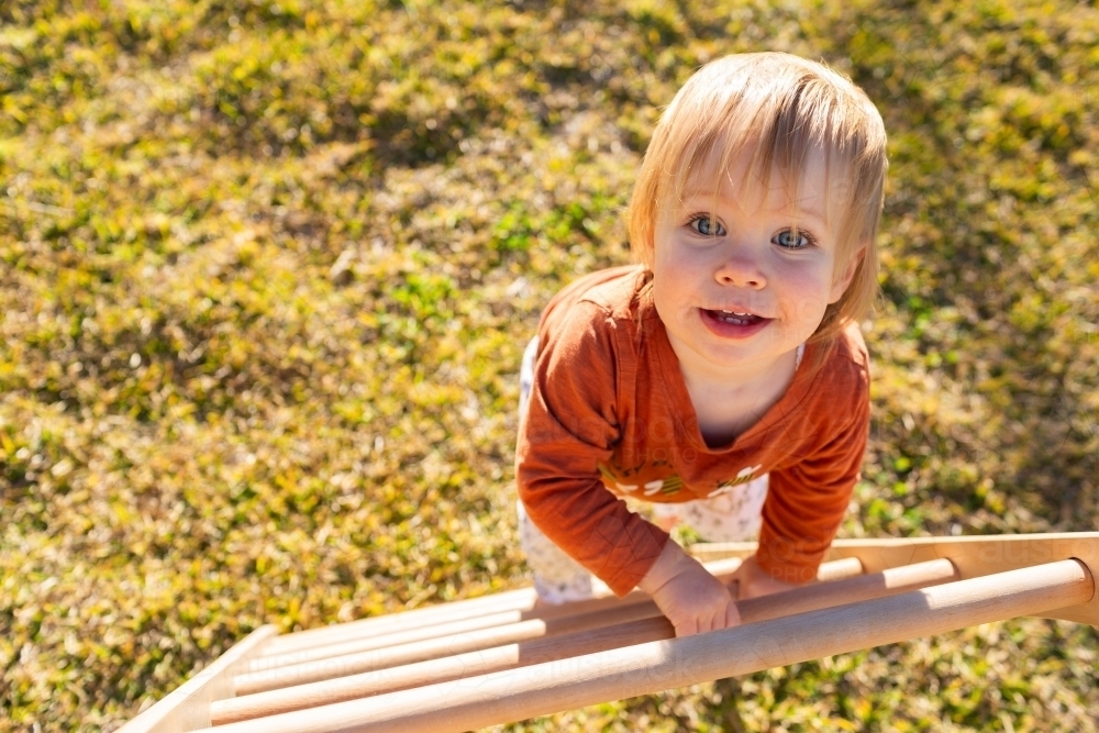 Toddler climbing up pikler triangle climbing frame in backyard - Australian Stock Image