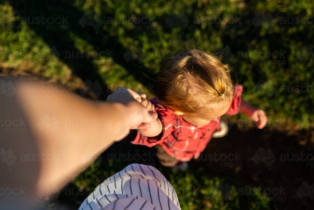 Toddler country kid holding mothers hand while going on walk around farm in late afternoon light - Australian Stock Image