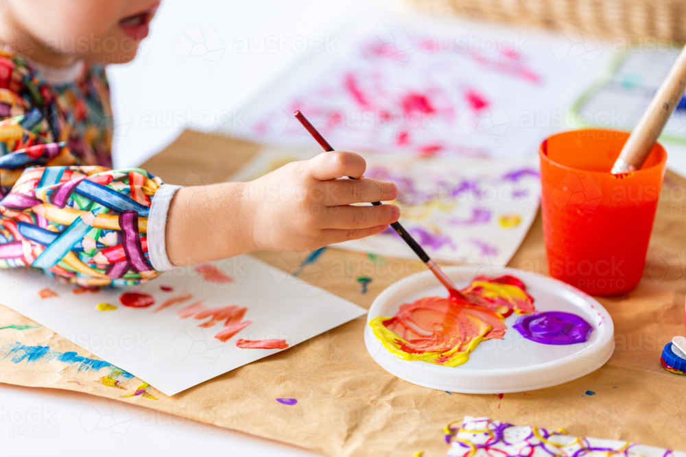 Toddler girl at home painting with coloured paint on paper - Australian Stock Image