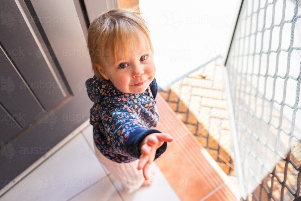 Toddler girl by front door step of house waiting to go outside for a walk with parent - Australian Stock Image