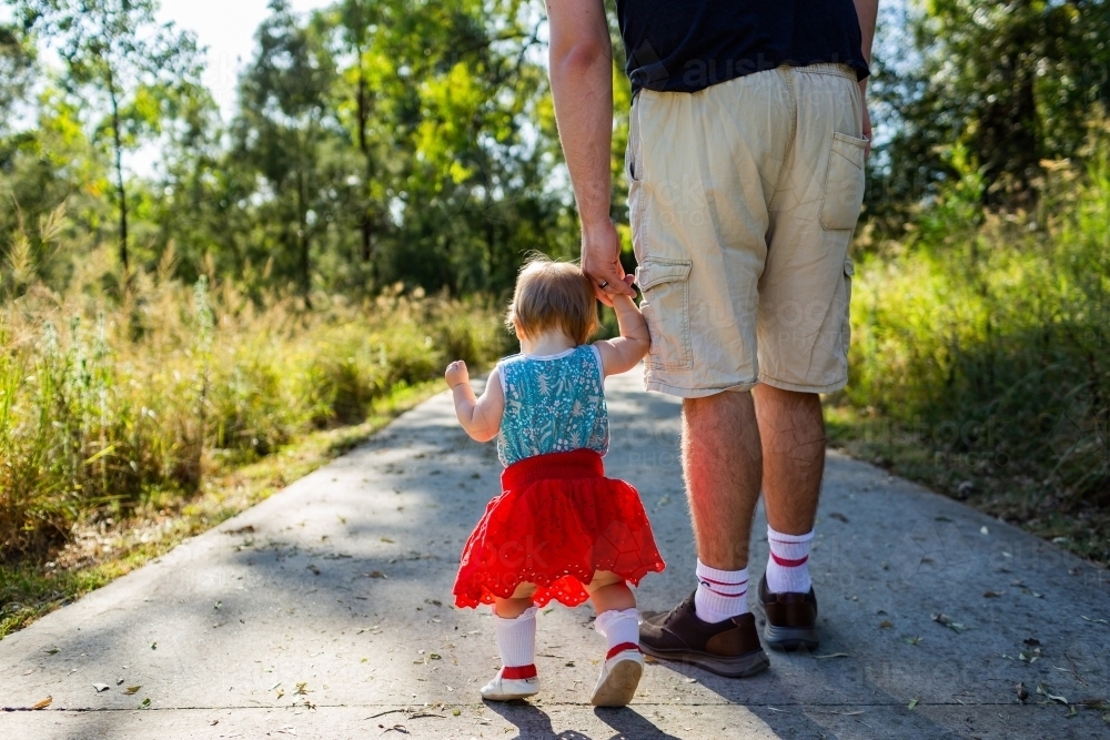 Toddler holding fathers hand walking down path in morning getting family exercise - Australian Stock Image