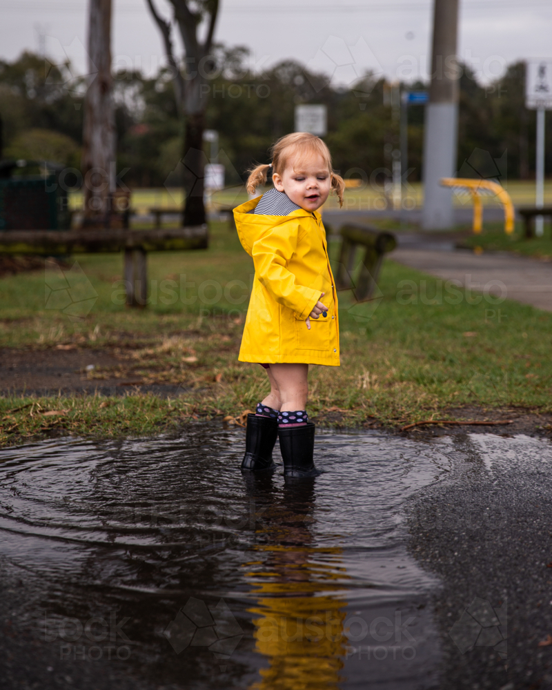 toddler in a yellow raincoat standing in a puddle - Australian Stock Image