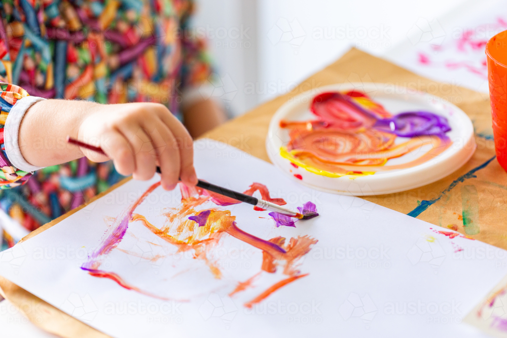 Toddler kid at home painting with coloured paint on paper - Australian Stock Image