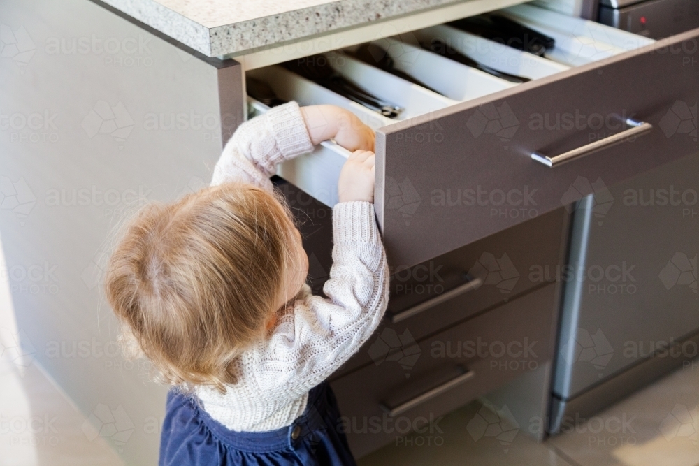 Toddler opening kitchen draw to get out spoon - Australian Stock Image