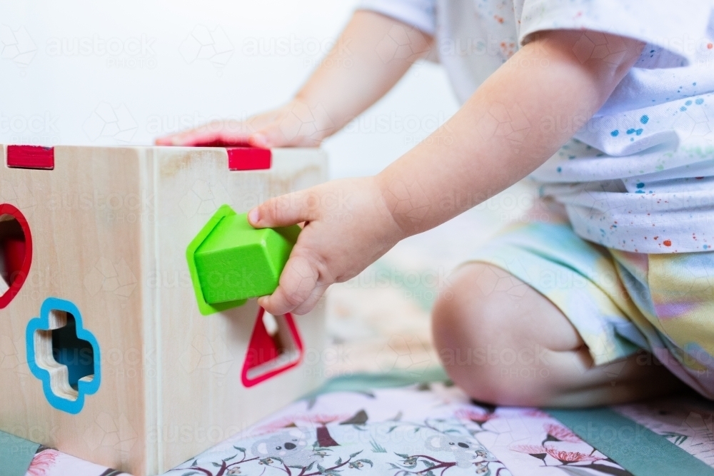 Toddler posting coloured shapes into wooden shape sorter box - Australian Stock Image