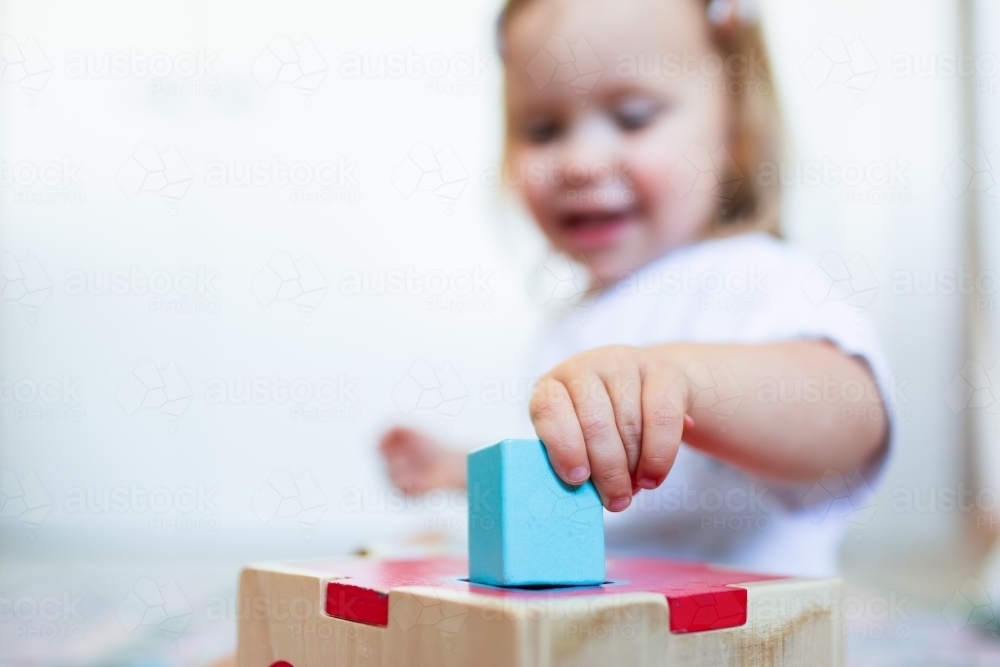 Toddler posting coloured shapes into wooden shape sorter box - Australian Stock Image