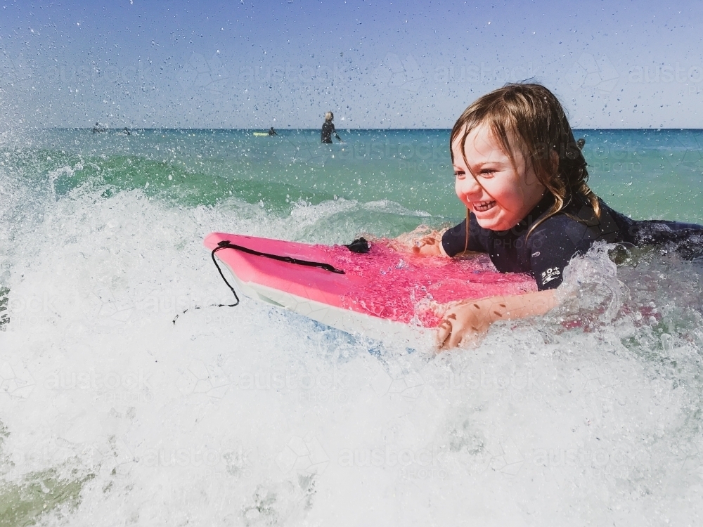 Toddler surfing a wave on a pink boogey board - Australian Stock Image