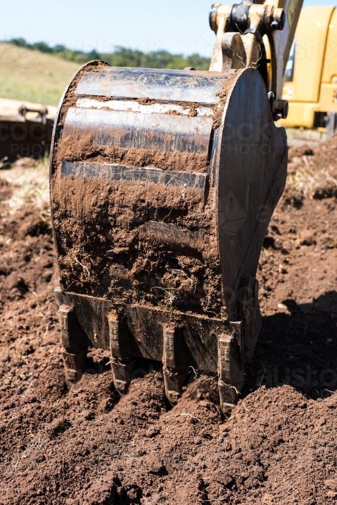 Toothed excavator bucket digging in brown soil - Australian Stock Image