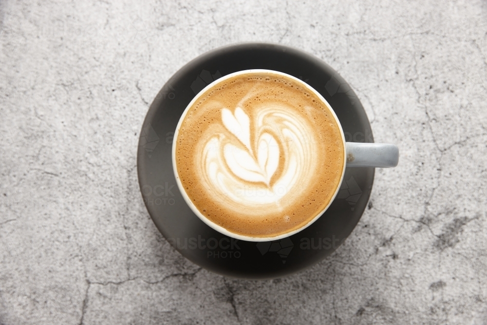 Top-down shot of flat white in mug on black saucer - Australian Stock Image