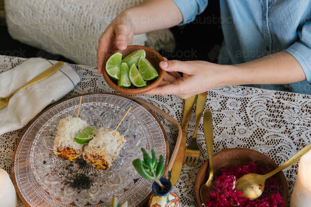 Top-down view of a table with various food and woman holding a small bowl of lime - Australian Stock Image