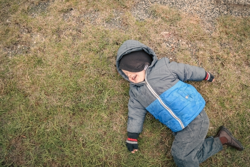 Image of Top down view of little boy lying on grass in winter with ...