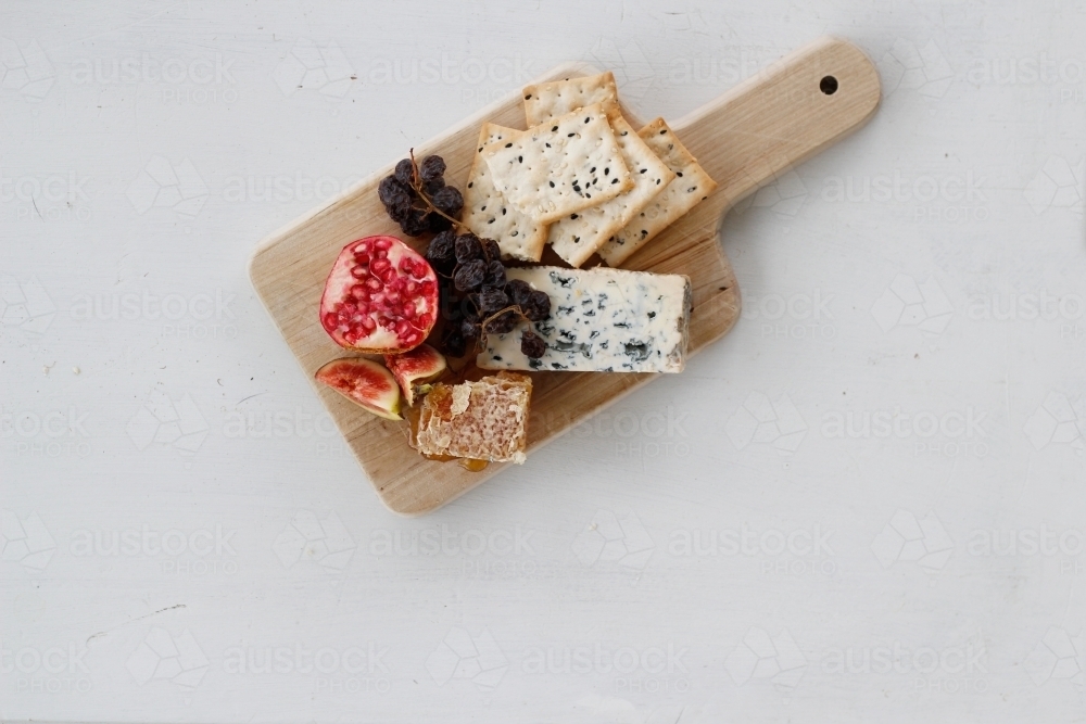 Top down view of wooden cheese board with cheese, crackers, pomegranate, figs and muscatels - Australian Stock Image