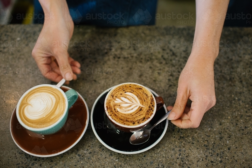 Top shot of a barista's hands serving artistic coffees - Australian Stock Image