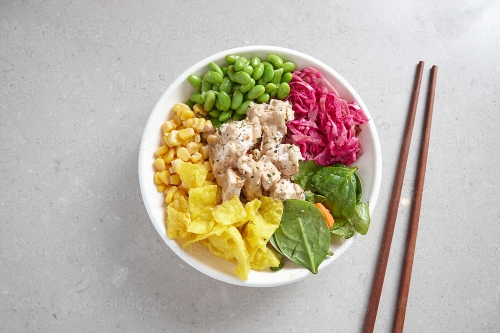 top shot of a bowl of chicken vegetable salad with wooden chopsticks on top grey background - Australian Stock Image