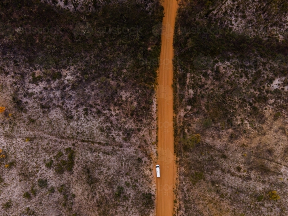 top shot of a white car on a long narrow dirt road surrounded by trees and bushes - Australian Stock Image