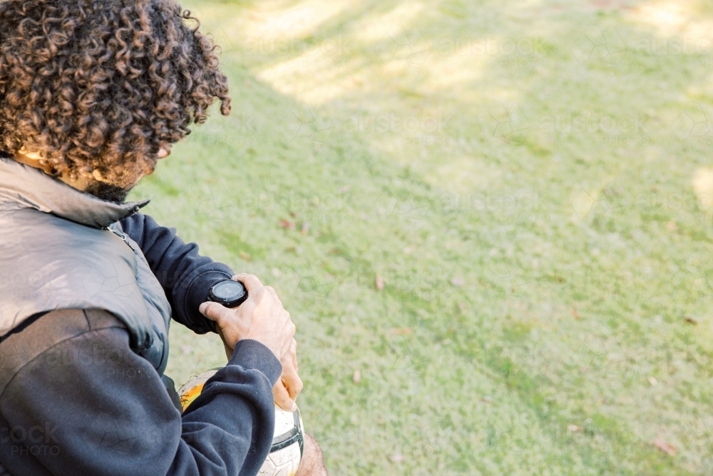 Top view shot of a man with curly hair and with a soccer ball touching and looking at his watch - Australian Stock Image