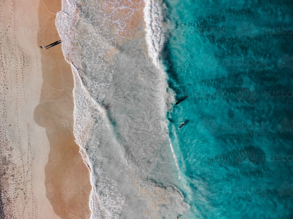 top view shot of a person standing on a white sand shore with sea waves on a sunny day - Australian Stock Image