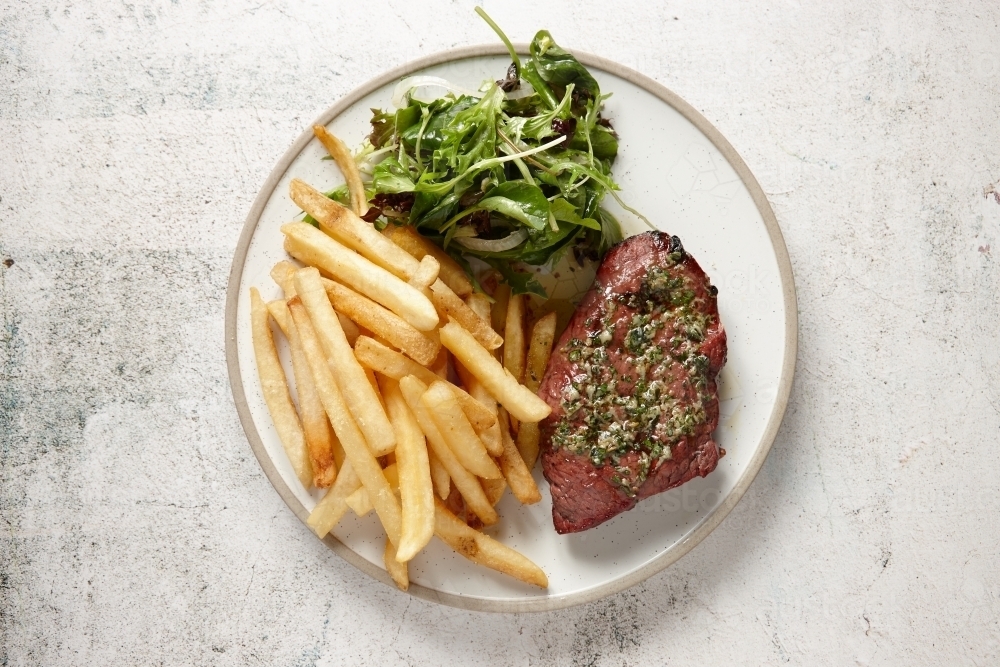 top view shot of a pork chop steak with fries and greens as sides all placed in a white plate - Australian Stock Image