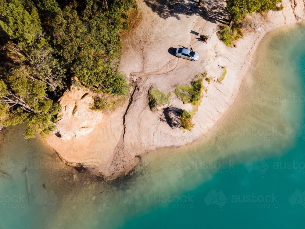 top view shot of blue water with green trees and white rock formation with a parked car - Australian Stock Image