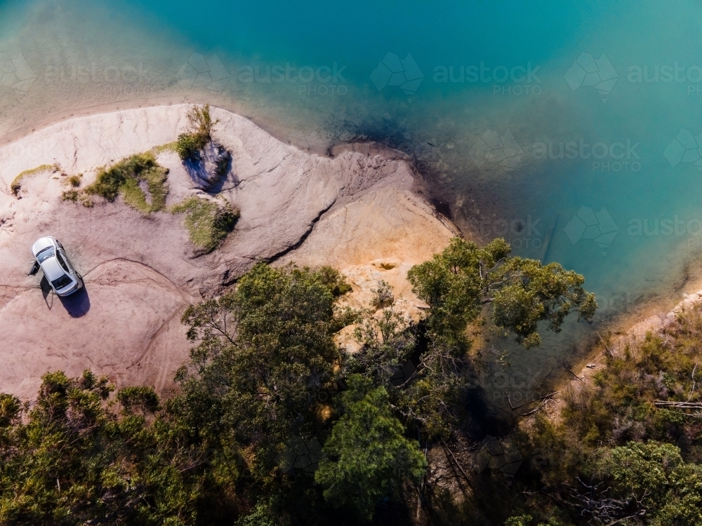 top view shot of blue water with green trees and white rock formation with a parked car - Australian Stock Image