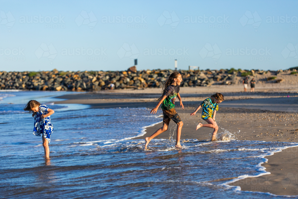 Torres Strait Islander children playing together at beach on windy day - Australian Stock Image