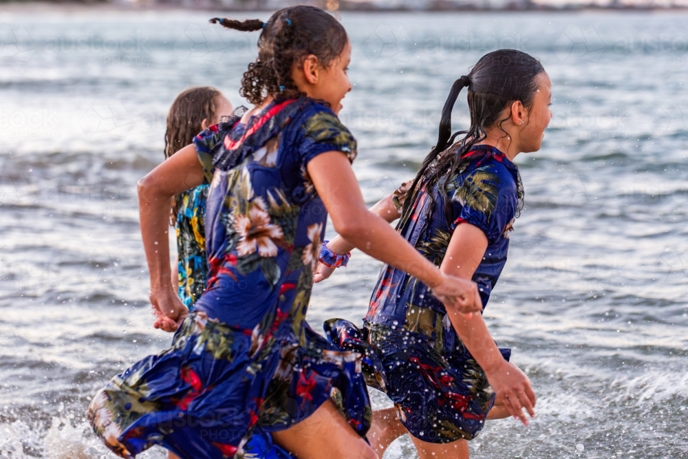 Torres Strait Islander children running and splashing into ocean water at dusk on Australian coast - Australian Stock Image