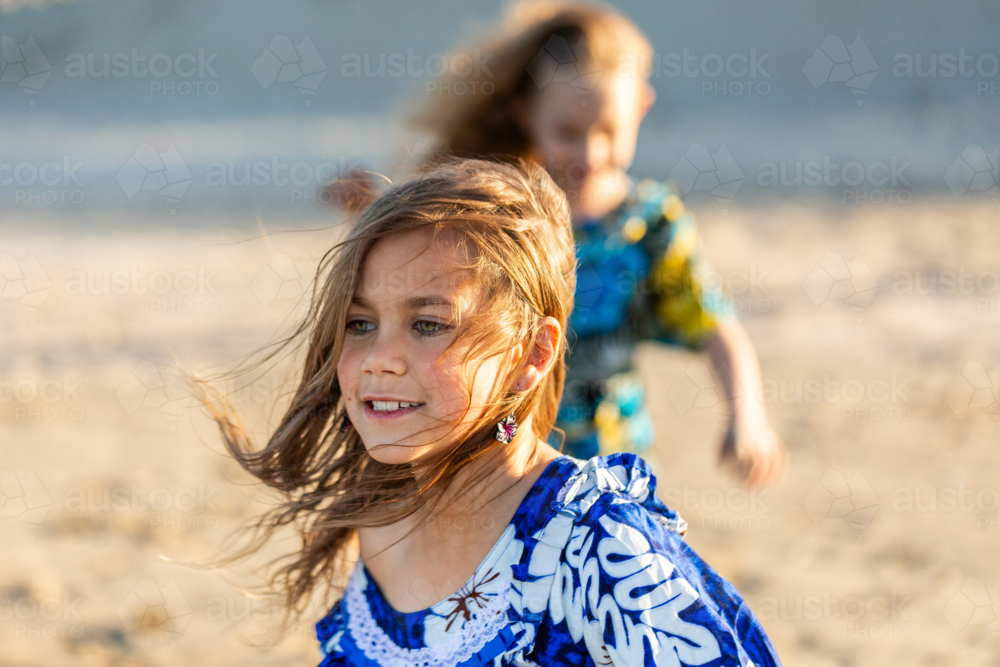 Torres Strait Islander girl at beach on windy day wearing traditional floral dress - Australian Stock Image