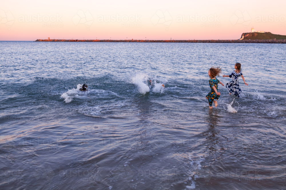 Torres Strait Islander girls in traditional floral dresses playing and splashing in ocean water - Australian Stock Image