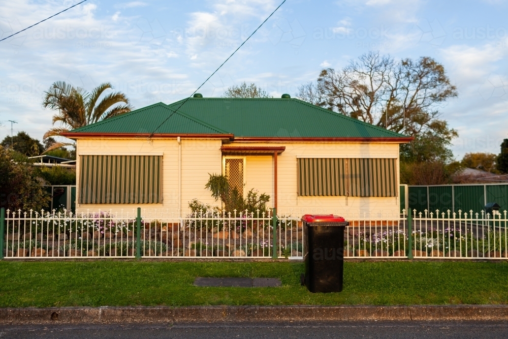 Town house with red rubbish bin awaiting collection by roadside in last light - Australian Stock Image