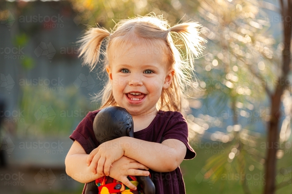 Toy Aboriginal Australian doll in colourful dress held by little girl outside - Australian Stock Image