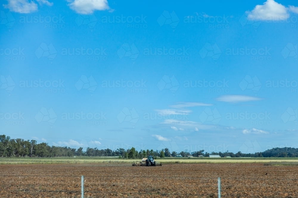 Tractor in farm paddock beside the road in country with big sky - Australian Stock Image